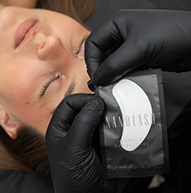 Kona með Hydrogel augnplástra slakar á á meðan tæknifræðingur setur á augnháralengingar